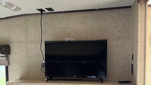 Uma TV sobre um aparador com gavetas, uma luminária no teto e um suporte para TV.