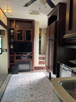 A kitchen with dark wood cabinets, a built-in TV, a stove, and a patterned rug. - Perfect 2-bedroom mobile home with AC in Punta Gorda (Punta Gorda)