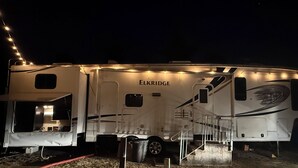 Uma grande RV com o nome 'ELKRIDGE' na lateral, equipada com uma área de cozinha, um banheiro pequeno e uma escada que leva ao deck superior.