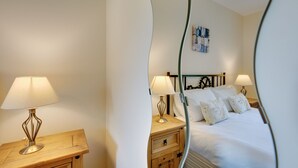 A hotel room with a bed, two bedside tables with lamps, a wooden nightstand, and a wall-mounted artwork.