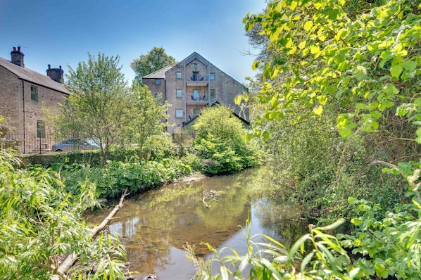 Een smalle waterweg omringd door weelderige begroeiing, met een gebouw met meerdere verdiepingen en balkons.