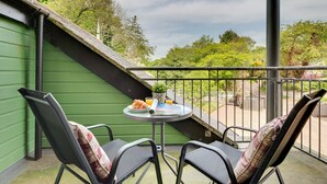 A balcony with two chairs, a table with breakfast, and a view of trees and a building.