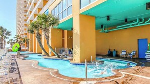 Ett hotellområde med en pool, solstolar och en byggnad med balkonger. Poolen har en böjd form.
