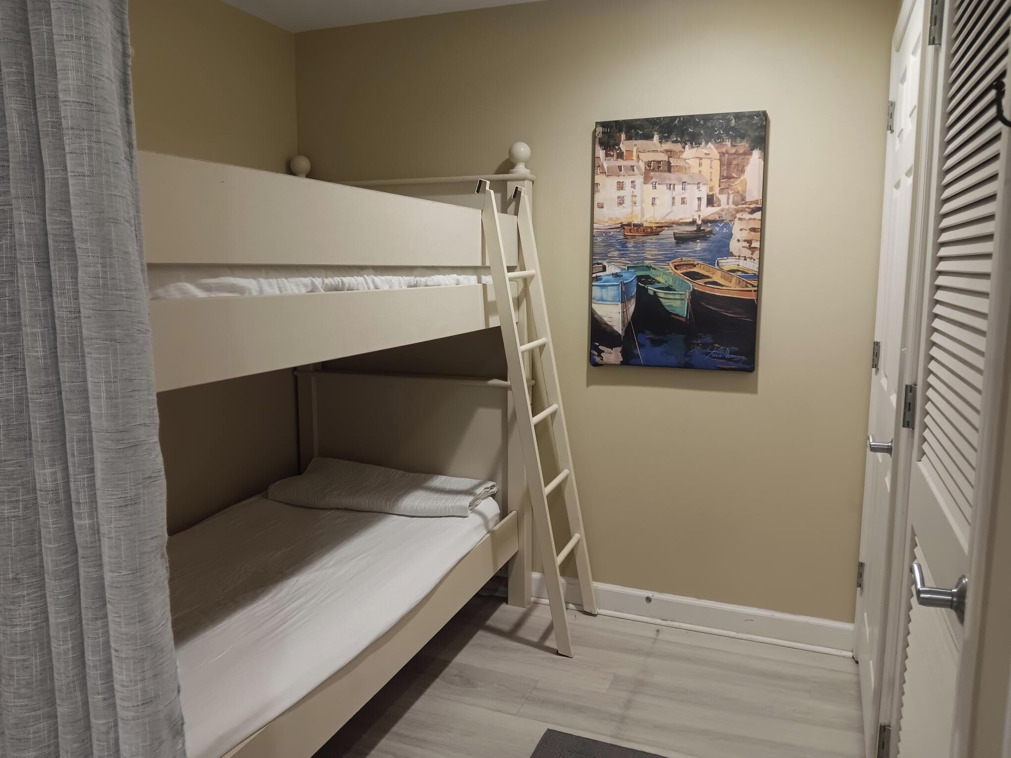 A bunk bed with a ladder, a painting of boats on a wall, and a door with a handle.