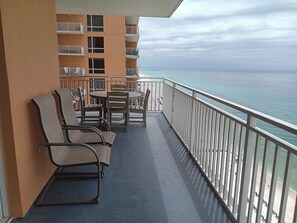 A balcony with chairs and a table, overlooking a beach and ocean.