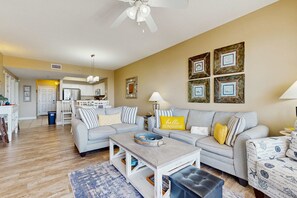 A living room with a sofa, coffee table, and a dining area with chairs. - Stylish condo with gulf views, pool and gym! (Miramar Beach)