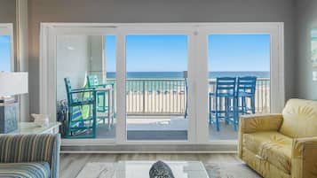 Un salon comprenant un canapé, un fauteuil, une table et donnant sur la plage grâce à une porte coulissante.