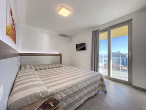 Ein Hotelzimmer mit einem Bett, einem Flachbildfernseher, einer Deckenleuchte und Blick auf die Stadt durch ein großes Fenster.
