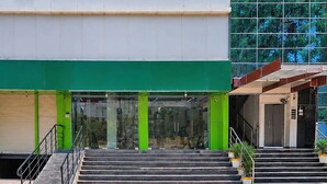 A building with a green awning, a staircase leading to a door, and a large glass window reflecting trees. - Deluxe Twin Room Gold Stone Comfort (Dehradun)