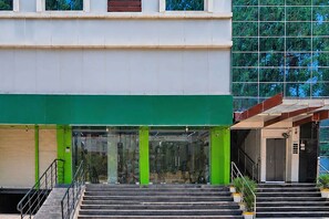 A building with a green awning, a staircase leading to a door, and a large glass window reflecting trees.