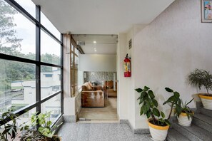 Habitación de hotel moderna con ventanas amplias, extintor y plantas en macetas.