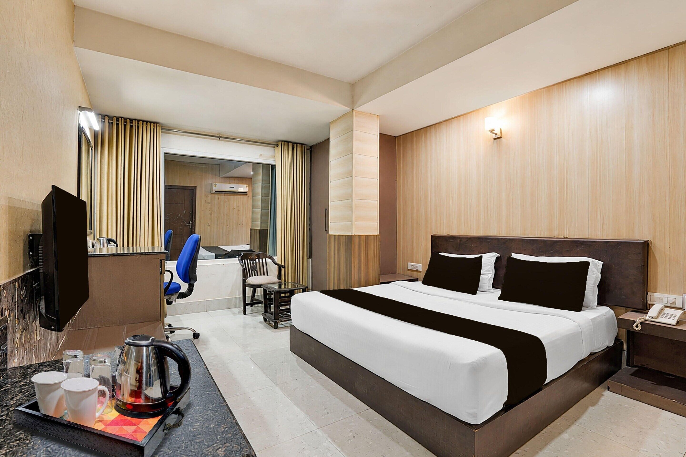 Una habitación de hotel con una cama, un escritorio con teléfono, cafetera y televisión.