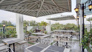 An outdoor patio area with white metal tables and benches, surrounded by potted plants and a white fence. - Deluxe Twin Room Gold Stone Comfort (Dehradun)