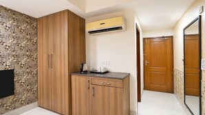 A compact kitchen with wooden cabinets, a built-in air conditioner, and a countertop with a kettle and cups. - Deluxe Twin Room Gold Stone Comfort (Dehradun)