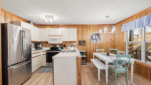 Una cocina compacta con refrigerador, microondas y lavamanos, paredes de madera, y un comedor con sillas y una mesa.