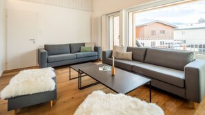 Un salon moderne avec un canapé gris, une table basse et un pouf blanc à la texture douce et duveteuse.