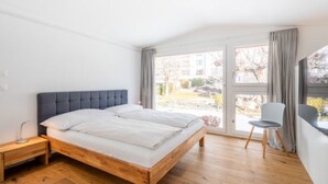 Une chambre à coucher avec un lit, un plancher en bois, une chaise et une fenêtre avec des rideaux.