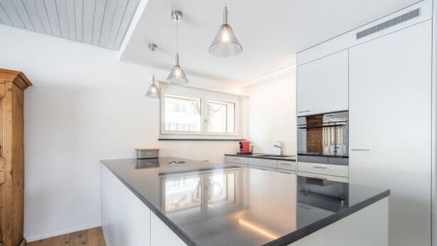 Une cuisine moderne dotée d’un îlot central, de luminaires suspendus et de meubles blancs.