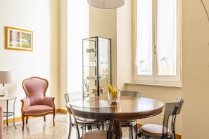 A dining area with a round table, chairs, a glass cabinet, a vase with flowers, a chair, a lamp, and a window with curtains. - Elegant apartment of 66 sqm can accommodate up to 4 people, located on the third floor of a period building with a lift (4 steps to access). The property is located in the historic center of Livorno, just 3 minutes walk from the Duomo and a short walk fr (Livorno)