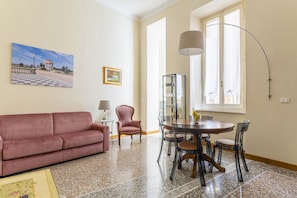 Ein Wohnzimmer mit einem rosafarbenen Sofa, einem Esstisch mit Stühlen, einer Lampe und einem Gemälde an der Wand.