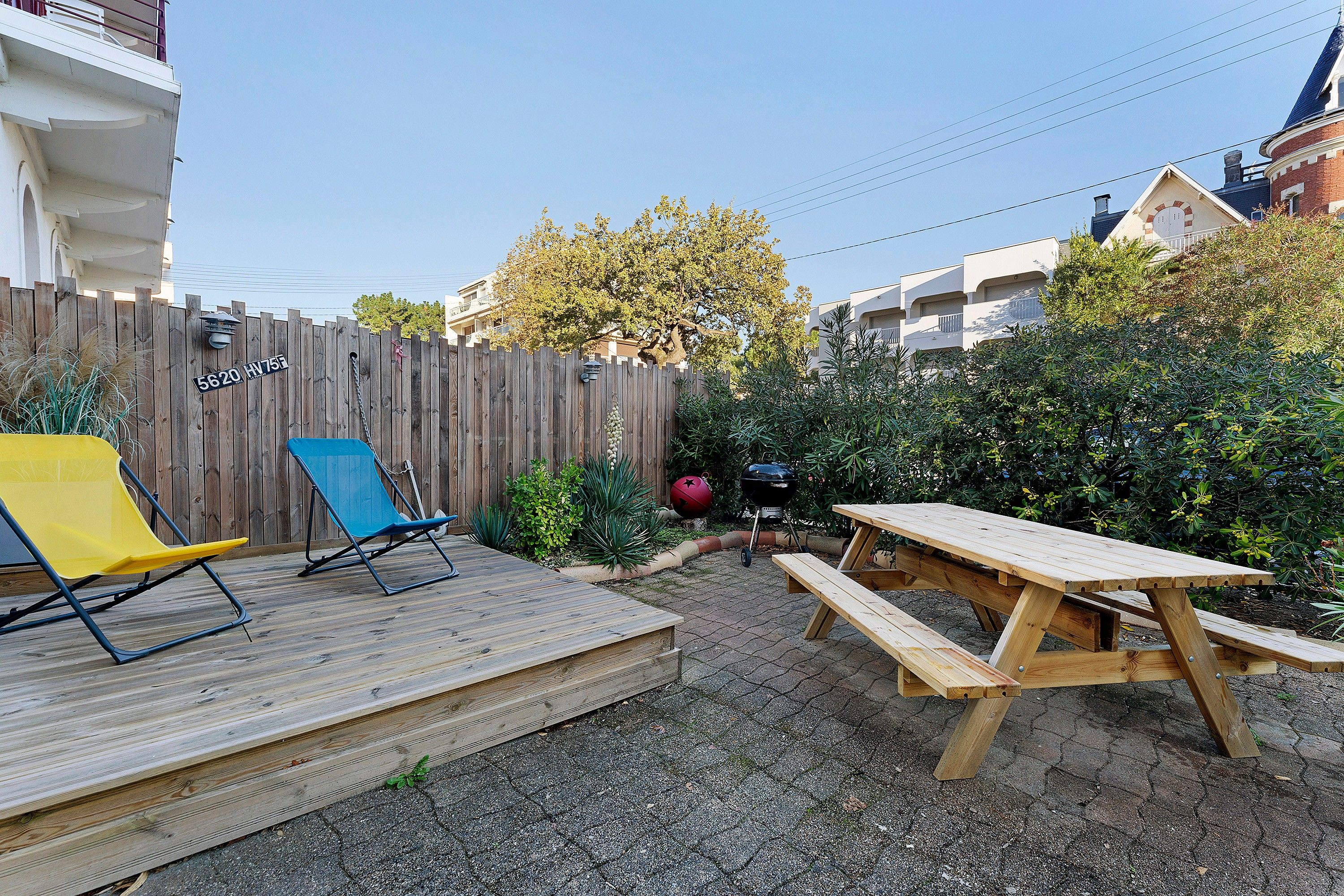 A backyard with a wooden deck, a picnic table, and a blue chair.