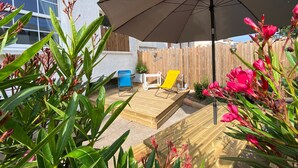 Un área de patio con cubierta de madera, un paraguas grande y una silla blanca.
