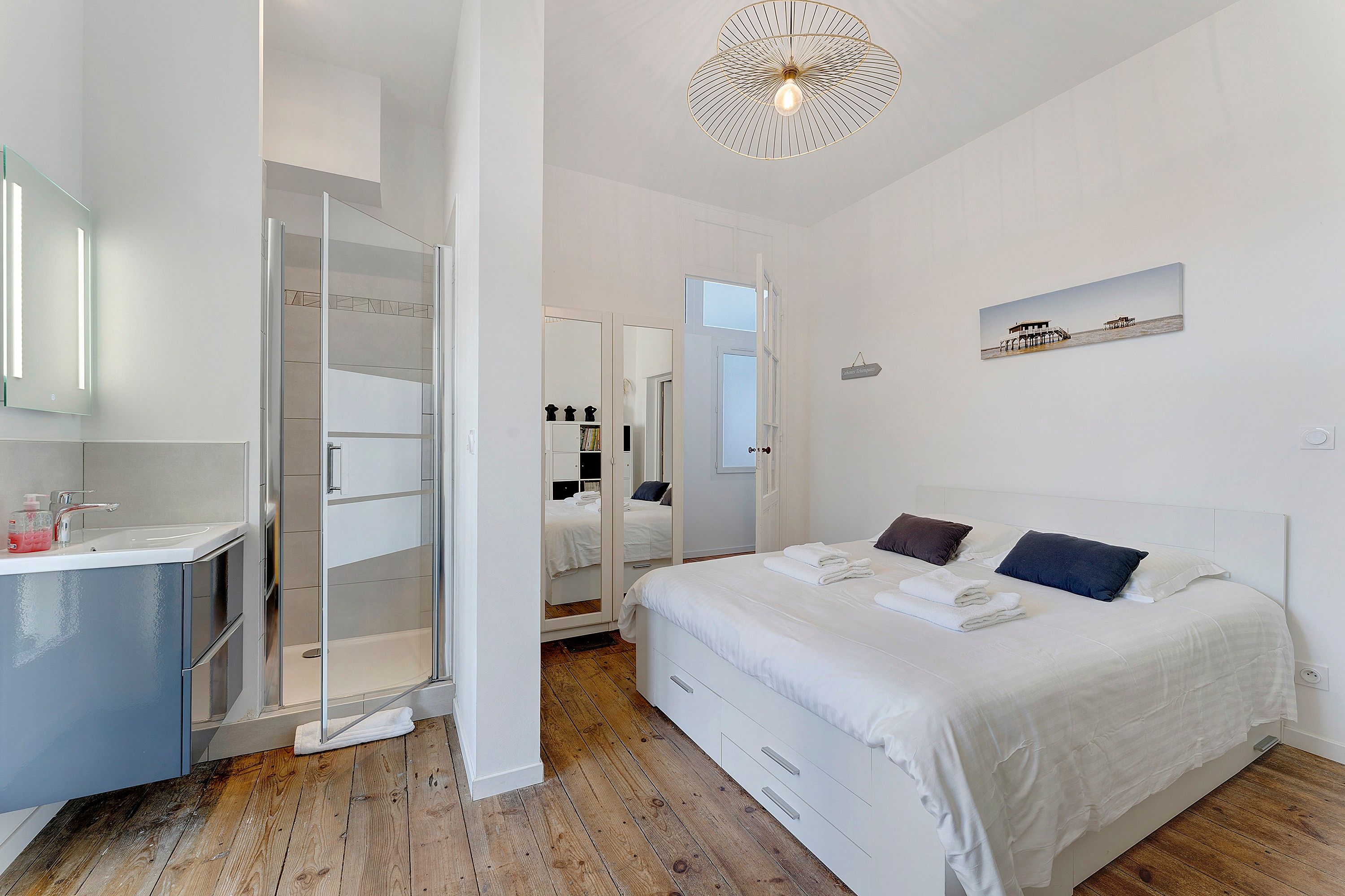A modern bedroom with a large bed, a walk-in closet, and a bathroom with a glass shower enclosure.