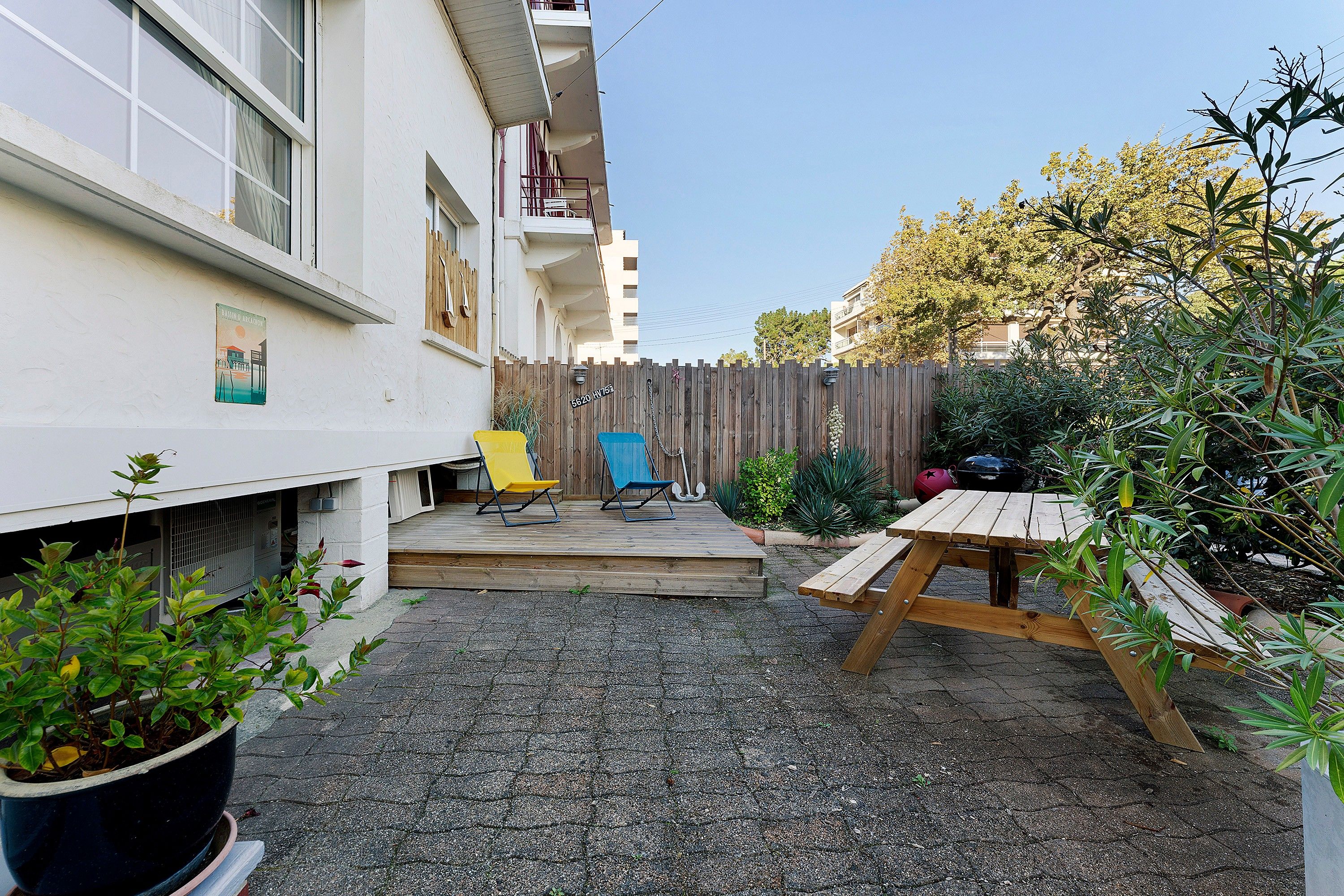 A residential backyard with a gravel patio, a wooden deck, a blue door, and a wooden fence.