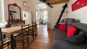 Un comedor con una mesa y sillas de madera, un espejo con marco rojo y una escalera que lleva a otra habitación.