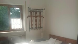 Une chambre avec deux lits, un radiateur, une fenêtre avec un rideau et une étagère métallique fixée au mur.