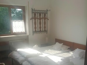 A room with two beds, a radiator, a window with a curtain, and a wall-mounted metal rack. - Allgäu Vibes-OberstaufenPLUS, train station access, view, protected balcony (Oberstaufen)