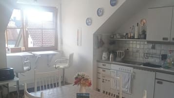 Eine Küche mit weißen Schränken, einem Esstisch mit Stühlen, einem Fenster mit Jalousien und einem Deckenventilator.