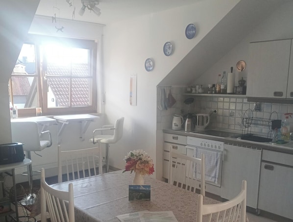 A kitchen with white cabinets, a dining table with chairs, a window with blinds, and a ceiling fan. - Allgäu Vibes-OberstaufenPLUS, train station access, view, protected balcony (Oberstaufen)