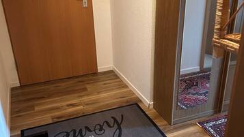 Eine Holztür, ein an der Wand befestigtes Stromdosenfeld, eine Fußmatte mit dem Text 'Welcome' und ein gemustertes Teppich.