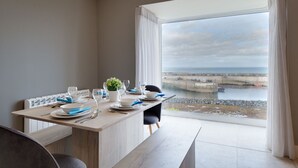 Un coin repas avec vue sur la mer, une table dressée avec des assiettes, des verres et une petite plante.