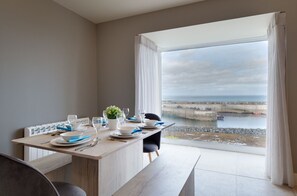 A dining area with a view of the sea, a table set with plates, glasses, and a small plant. - Seal`s Bay Luxury Holiday Home for 4 in Seahouses (Northumberland)