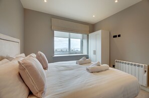A bedroom with a large bed, a window with a view, a radiator, and a wardrobe. - Seal`s Bay Luxury Holiday Home for 4 in Seahouses (Northumberland)
