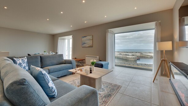 Un salon spacieux, doté d’un grand canapé, d’une table basse et offrant une vue sur la mer grâce à une grande fenêtre.