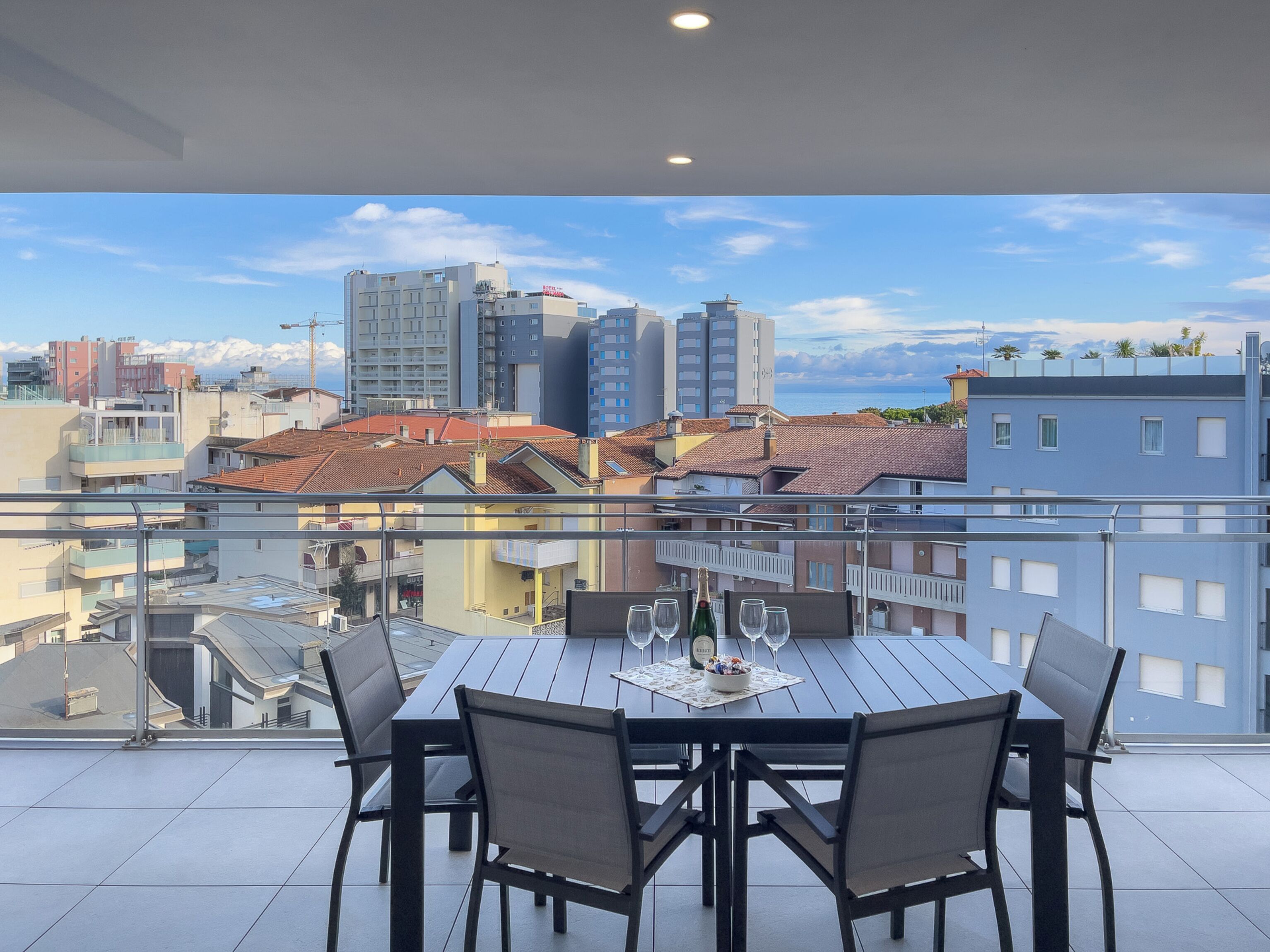 A balcony with a table set for dining, overlooking a cityscape with buildings and a clear sky.