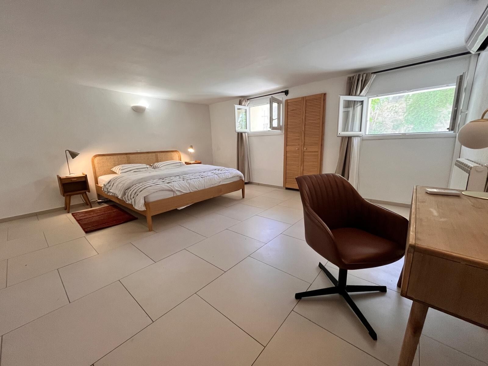 A bedroom with a bed, bedside table, lamp, chair, desk, window, and wardrobe.