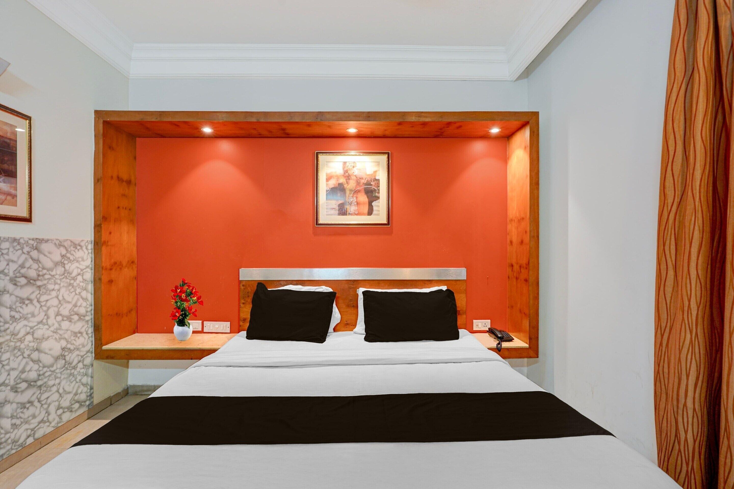 Habitación de hotel con una cama, una mesita de noche, un jarrón con flores y un cuadro en la pared.