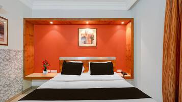Habitación de hotel con una cama, una mesita de noche, un jarrón con flores y un cuadro en la pared.