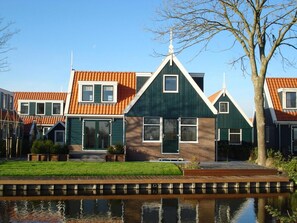 A row of traditional houses with gabled roofs, a wooden dock, and a calm water body in front. - Detached Holiday Home for 10 Guests (West-Graftdijk)