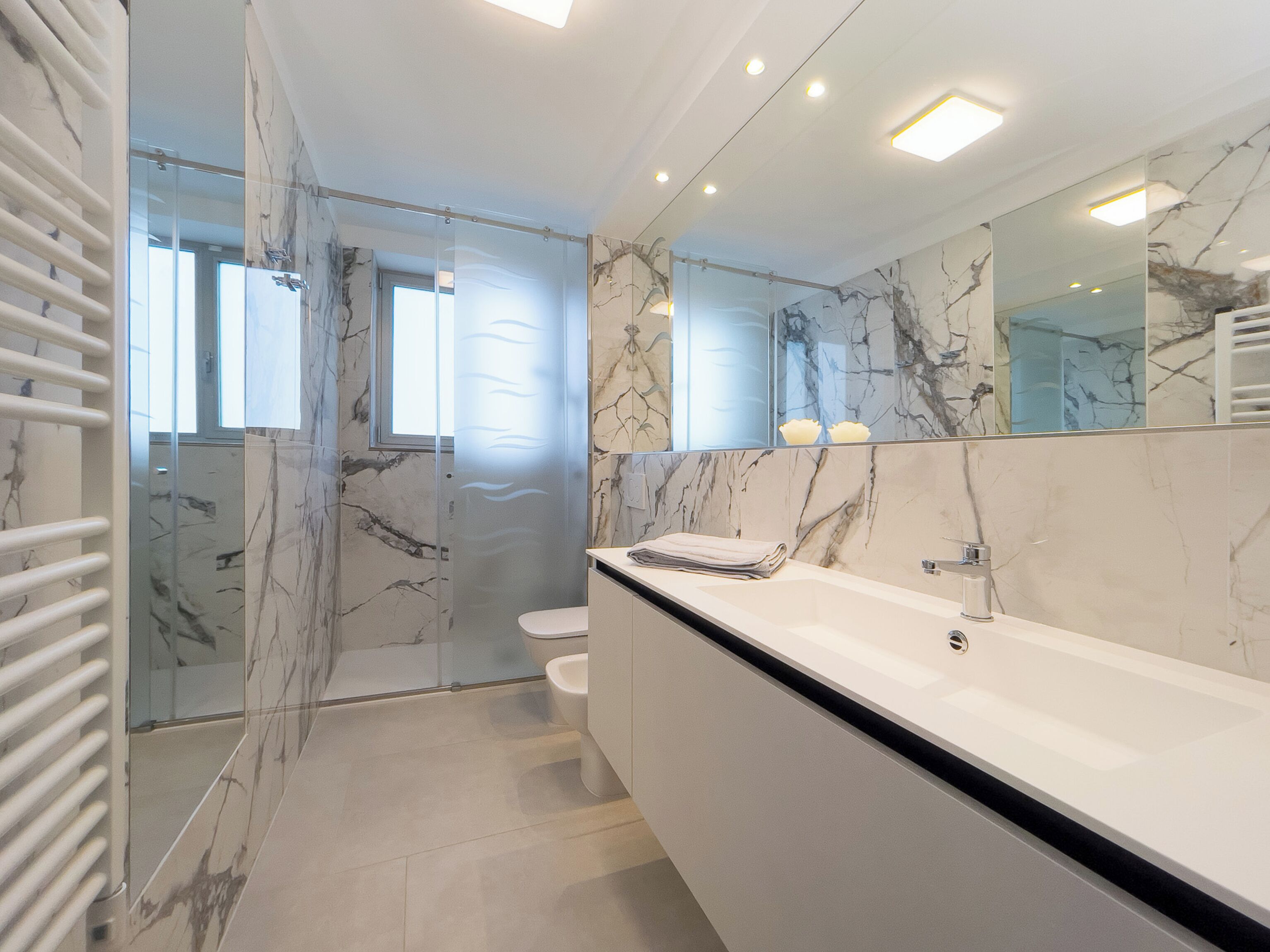 Un baño moderno con cabina de ducha de vidrio, un lavabo blanco y un espejo grande.
