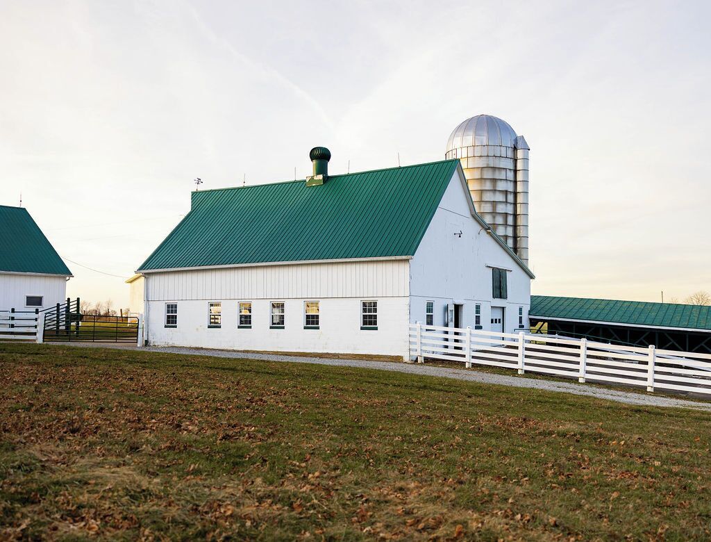 A white barn with a green roof and a silo.