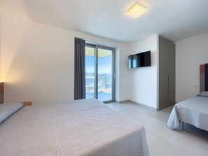 A hotel room with two beds, a TV, a sliding glass door to the outside, and a ceiling light. - Lignano Penthouse Near Beach (Lignano Sabbiadoro)