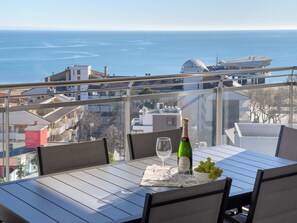 A balcony with a table set for two, a bottle of wine, and a bowl of grapes. - Lignano Penthouse Near Beach (Lignano Sabbiadoro)