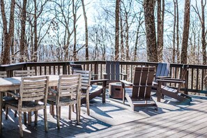 Une terrasse en bois, agréée de mobilier d’extérieur, notamment des chaises et des tables, et entourée d’arbres.