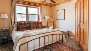 A bedroom with a bed, bedside tables, a desk, a chair, a ceiling fan, and a large wooden door. - Mountain Retreat: Year-Round Getaway, Pup Friendly (Wintergreen Resort)