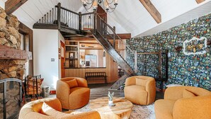 A spacious living area with a stone fireplace, a wooden staircase, and a colorful floral wall. - Mountain Retreat: Year-Round Getaway, Pup Friendly (Wintergreen Resort)